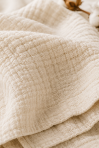 Etoffe double gaze de coton beige gaufrée posée avec une branche de coton brut à côté
